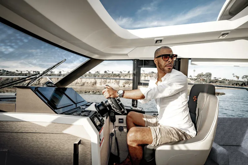 Slide: The Image of Man steering a 2025 Prestige 420S yacht, wearing sunglasses, in a sunny setting. - 5