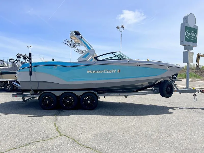 Slide: The Image of 2023 MasterCraft X24 boat on trailer, blue and gray design, parked outdoors. - 20