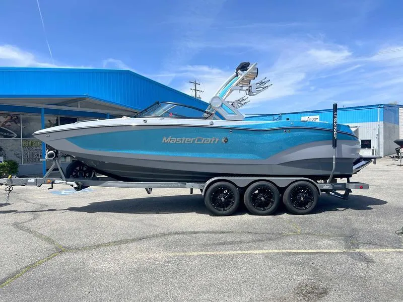 Slide: The Image of 2023 MasterCraft X24 boat on trailer, parked outside a blue building under a clear sky. - 49