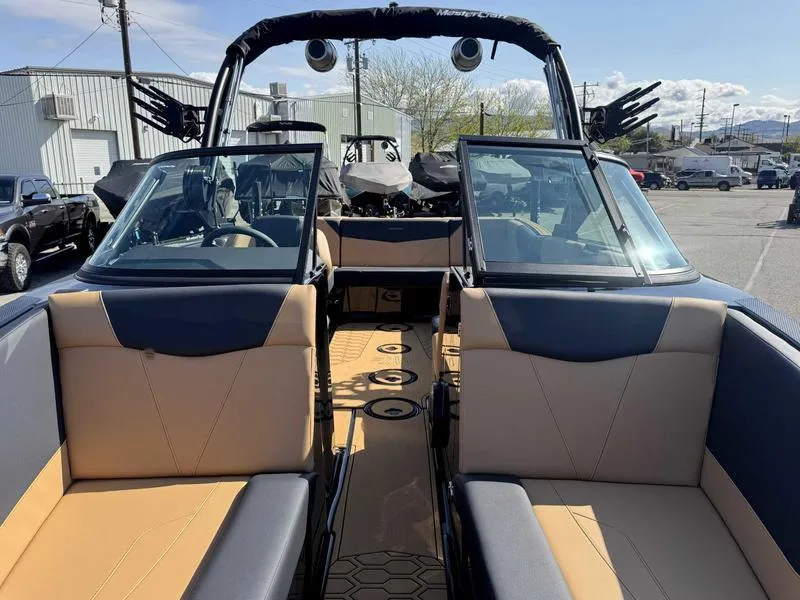 Slide: The Image of 2025 MasterCraft NXT22 boat interior with tan and black seating, open windshield, and tower speakers. - 13