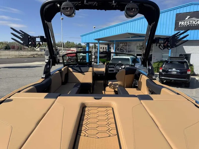 Slide: The Image of 2025 MasterCraft NXT22 boat interior with tan seating and black accents, parked at a dealership. - 7