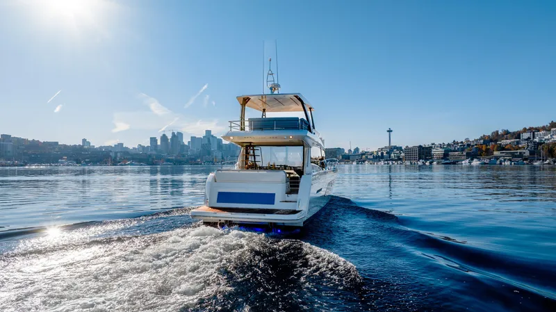 Slide: The Image of 2023 Prestige 520 yacht cruising on a sunny day with city skyline backdrop. - 2