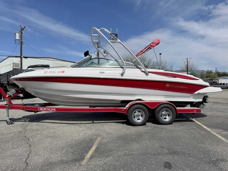 Slide: The Image of 2008 Crownline 230LS boat on a red trailer, parked outdoors under a clear sky. - 0