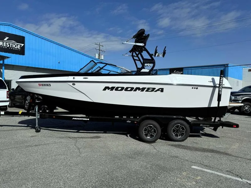 Slide: The Image of 2024 Moomba Max boat on trailer, parked outside a blue building under a clear sky. - 0