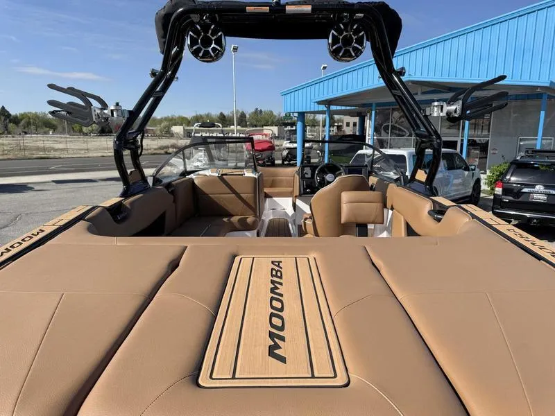 Slide: The Image of 2024 Moomba Max boat with tan interior, parked outdoors near a blue building. - 7