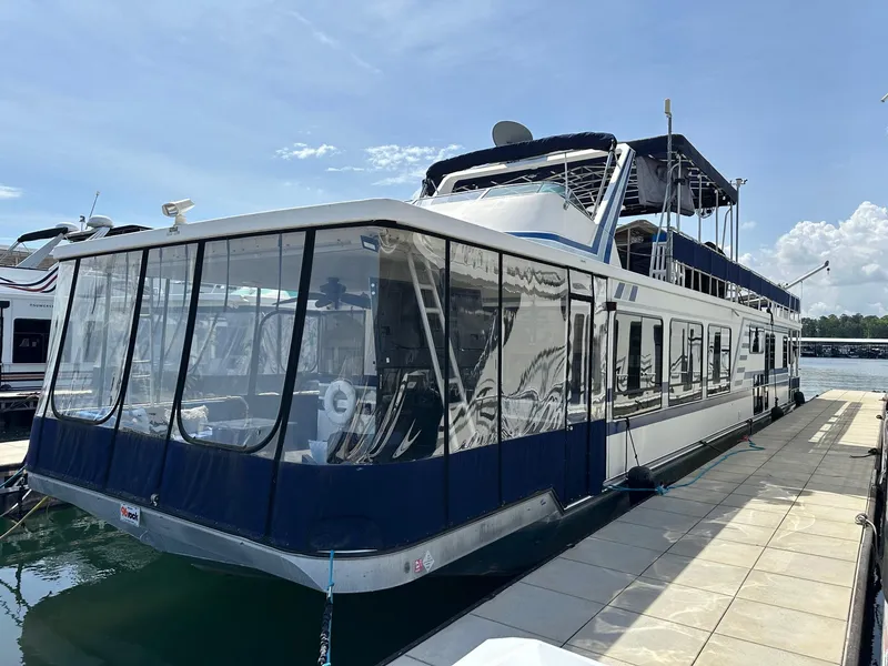 Slide: The Image of 1994 Sumerset 16x73 houseboat docked on a sunny day, featuring blue and white exterior. - 0