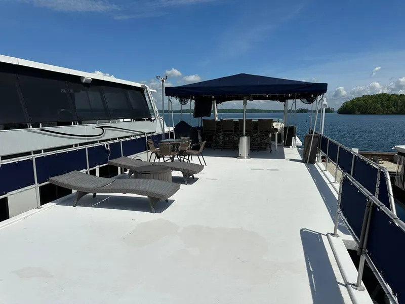 Slide: The Image of 1994 Sumerset 16x73 houseboat with spacious deck, lounge chairs, and canopy, set against a serene water backdrop. - 16