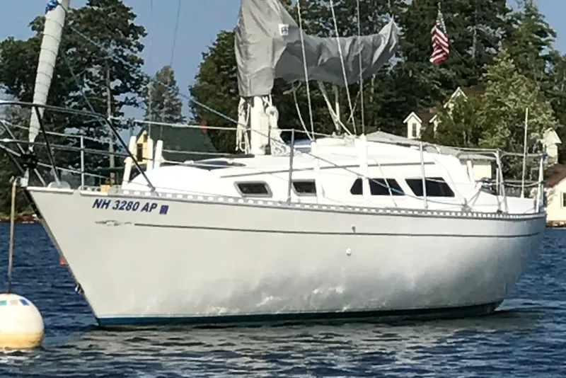 Slide: The Image of 1984 Islander 28 sailboat anchored on a calm lake with trees in the background. - 1
