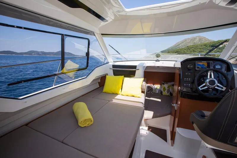 Slide: The Image of 2025 Jeanneau NC 795 interior with cozy seating, steering console, and scenic ocean view. - 16