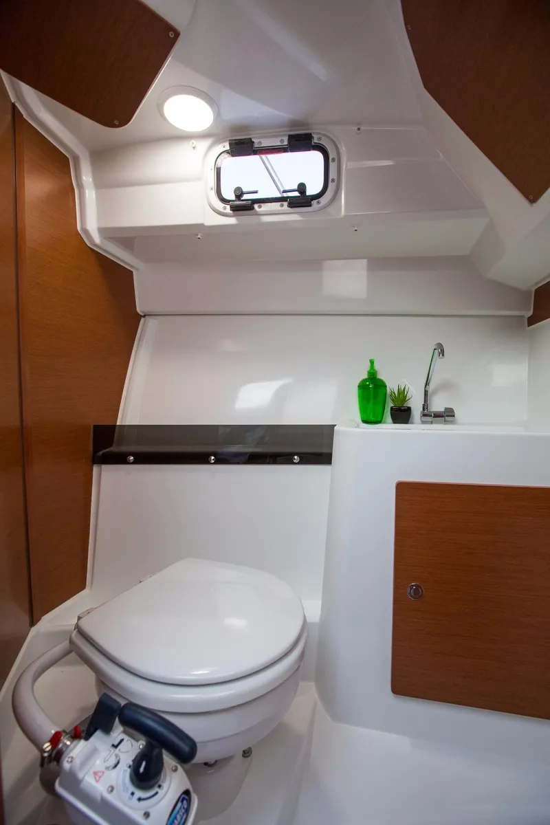 Slide: The Image of 2025 Jeanneau NC 795 boat bathroom with toilet, sink, and porthole window. - 11