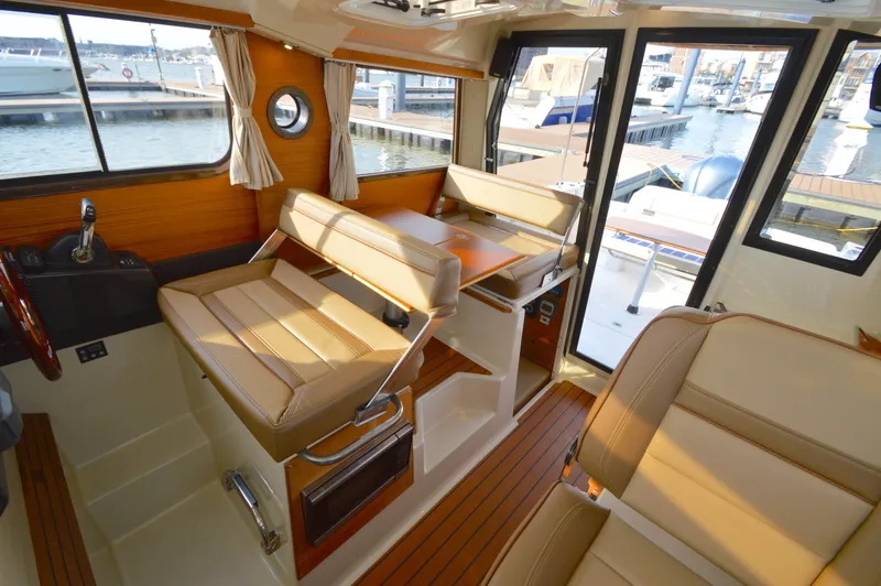 Slide: The Image of Interior of 2020 Ranger Tugs R-27 boat with tan seating and wood accents at a marina. - 18