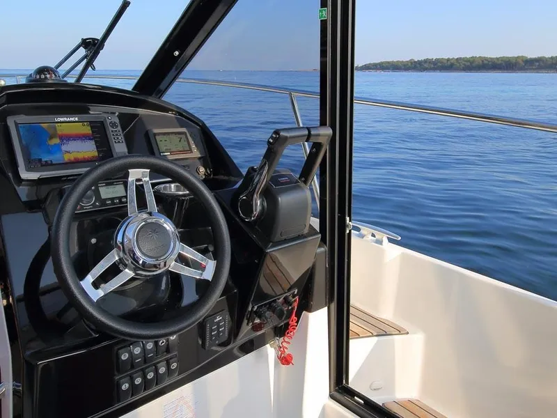 Slide: The Image of 2024 Jeanneau NC 895 helm with navigation screens, steering wheel, and ocean view. - 15