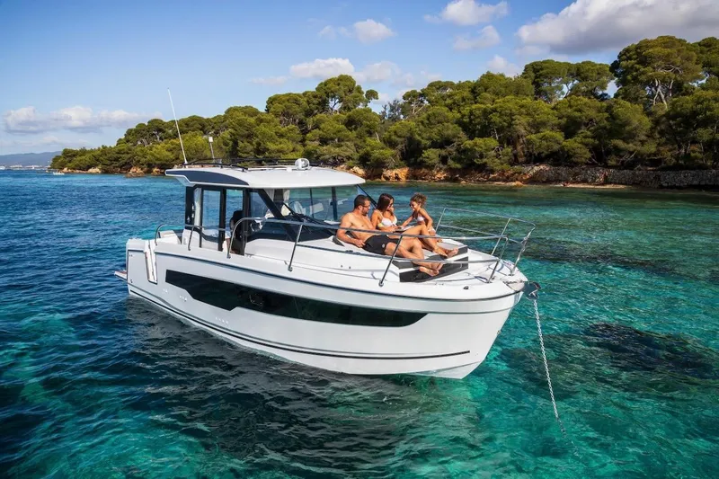 Slide: The Image of 2025 Jeanneau NC 895 Series 2 cruising in clear turquoise waters near a lush, green coastline. - 48