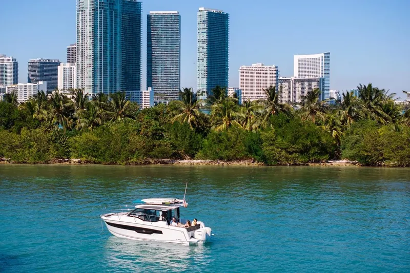 Slide: The Image of 2025 Jeanneau NC 895 Series 2 boat cruising near city skyline and lush greenery. - 77