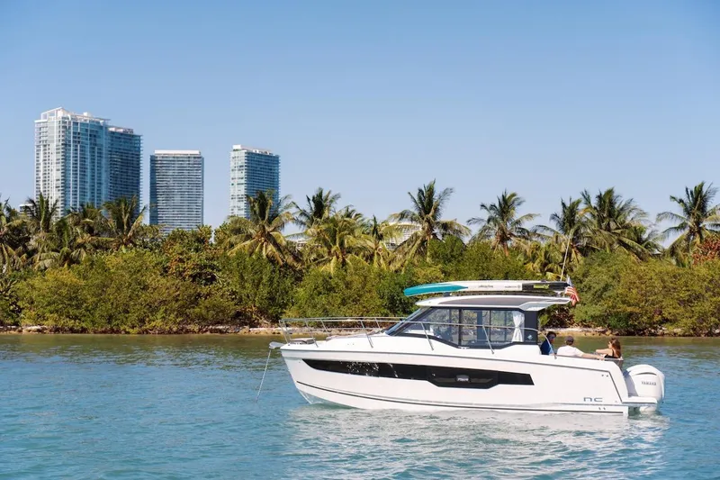 Slide: The Image of 2025 Jeanneau NC 895 Series 2 cruising near tropical shoreline with city skyline backdrop. - 85
