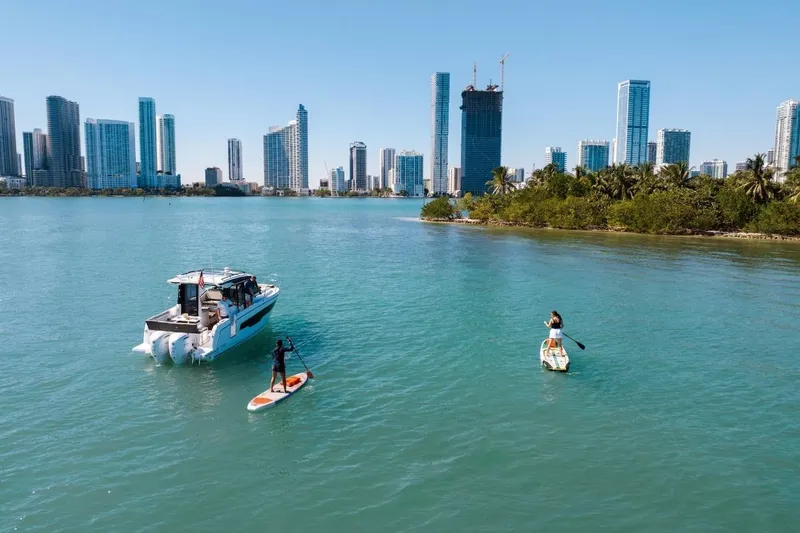 Slide: The Image of 2025 Jeanneau NC 895 Series 2 boat on water with paddleboarders, city skyline background. - 81
