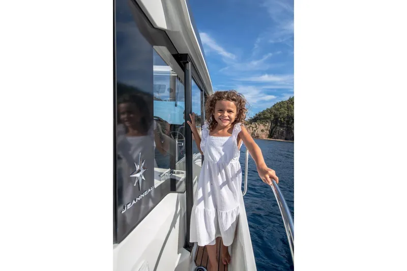 Slide: The Image of Young girl smiling on Jeanneau NC 895 Series 2 boat, 2025 model, with scenic ocean backdrop. - 57