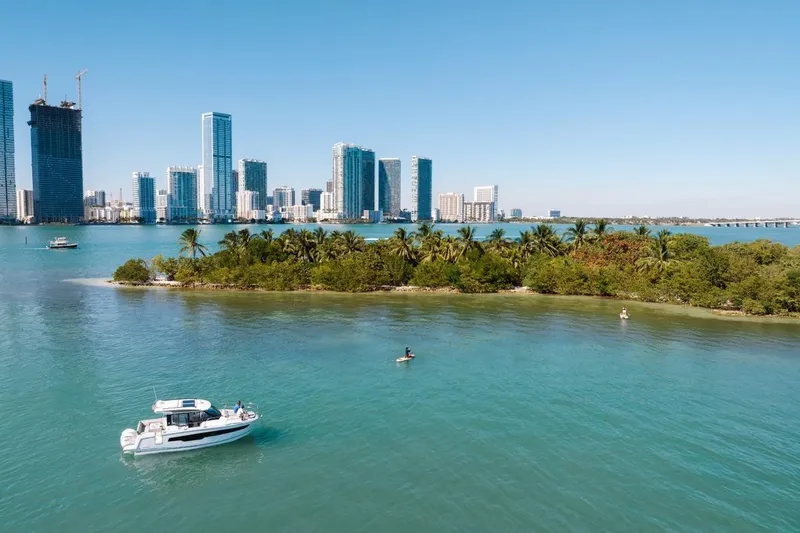 Slide: The Image of 2025 Jeanneau NC 895 Series 2 boat near tropical island with city skyline backdrop. - 80