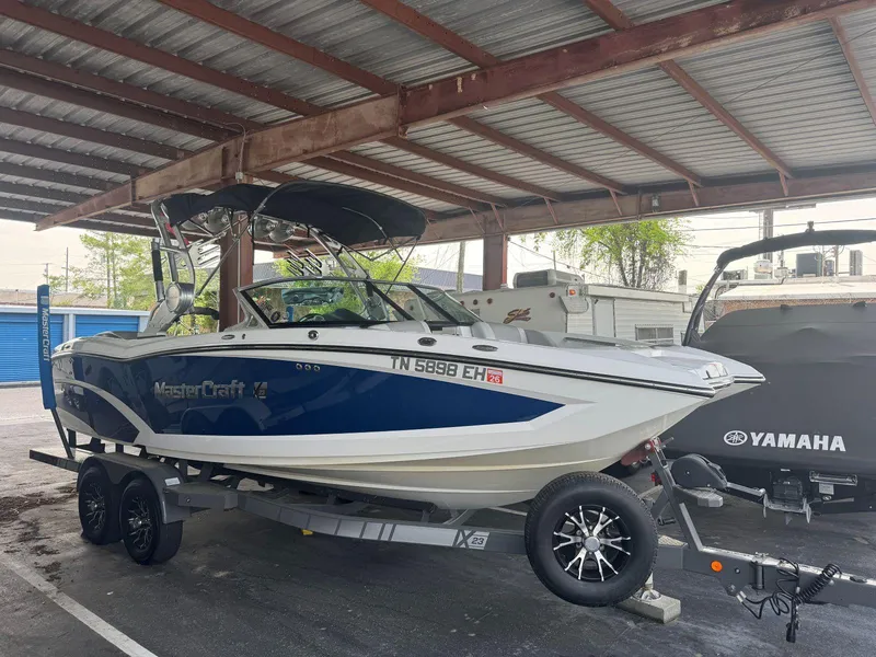 Slide: The Image of 2015 MasterCraft X23 boat on trailer under metal roof, parked beside Yamaha equipment. - 0