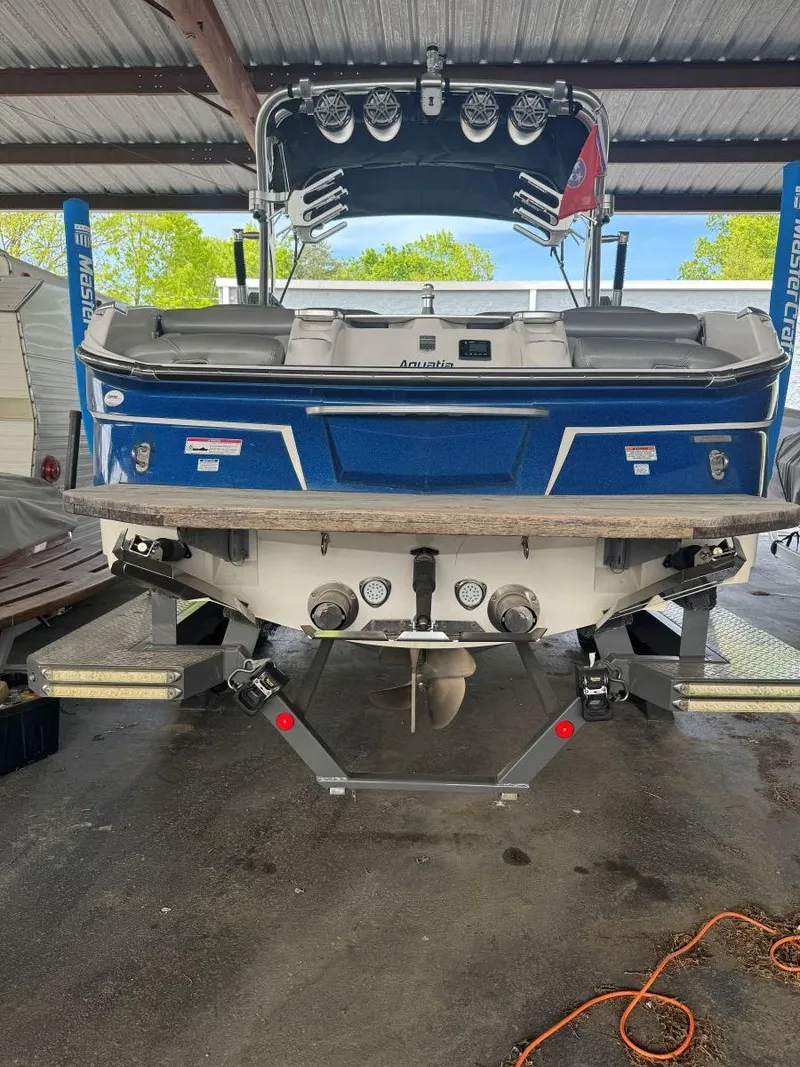 Slide: The Image of 2015 MasterCraft X23 boat in a covered dock, rear view with blue and white detailing. - 7