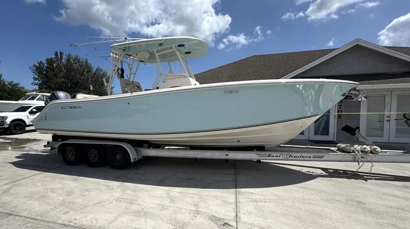 Slide: The Image of 2016 Cobia 296 Center Console boat on trailer, parked in driveway under blue sky. - 1