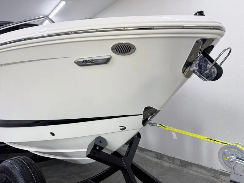 Slide: The Image of 2025 Chaparral 2870 SSX boat bow, sleek white design, displayed indoors on a trailer. - 49