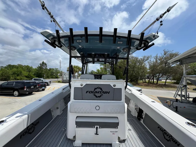 Slide: The Image of 2021 Fountain 38TE boat with fishing rods, parked outdoors under a partly cloudy sky. - 38