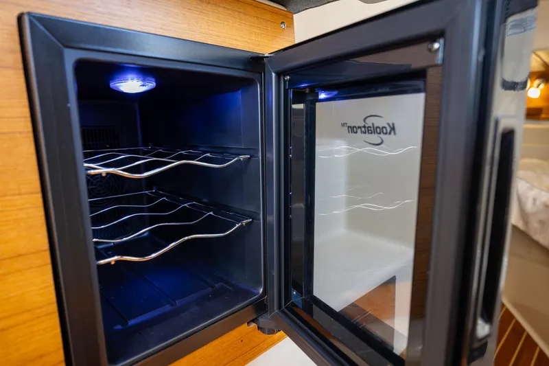 Slide: The Image of Open Koolatron fridge inside 2023 Ranger Tugs R-31 S boat, featuring wine racks and interior lighting. - 31