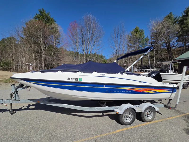 Slide: The Image of 2007 Bayliner 217 Deck Boat on trailer, parked outdoors with trees in background. - 1