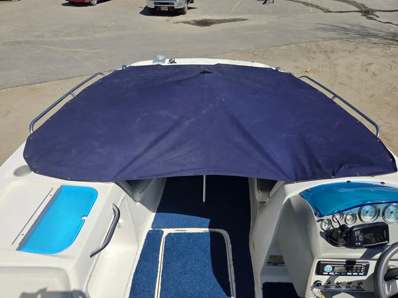 Slide: The Image of 2007 Bayliner 217 Deck Boat with blue cover and interior, parked on pavement. - 19