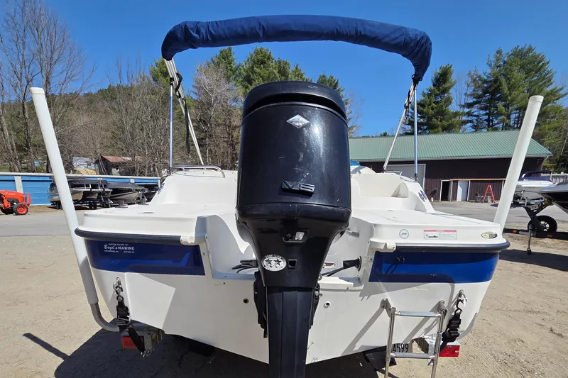 Slide: The Image of 2007 Bayliner 217 Deck Boat with outboard motor and blue canopy, parked outdoors. - 3