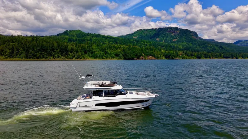 Slide: The Image of 2025 Jeanneau NC 1295 Fly cruising on a scenic lake with forested hills. - 2