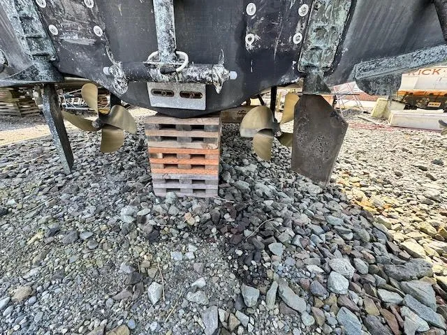 Slide: The Image of 2001 Maxum 3500 SCR boat on blocks, showing propellers and rudders on rocky ground. - 44