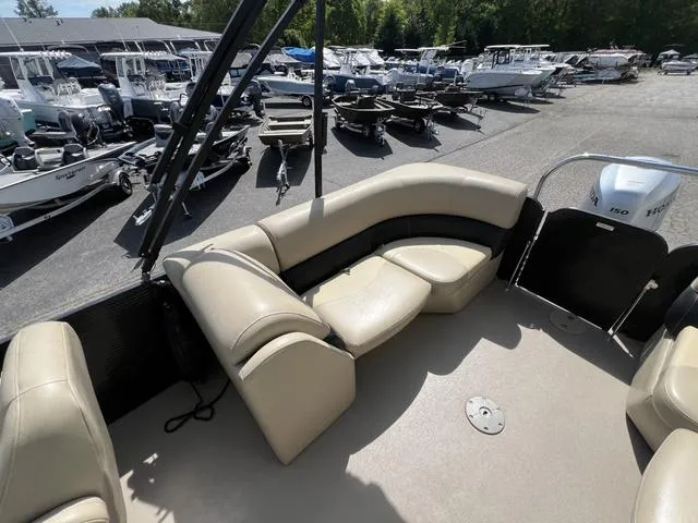 Slide: The Image of 2021 Manitou 23 Aurora LE VP pontoon boat interior with beige seating, docked among other boats. - 6