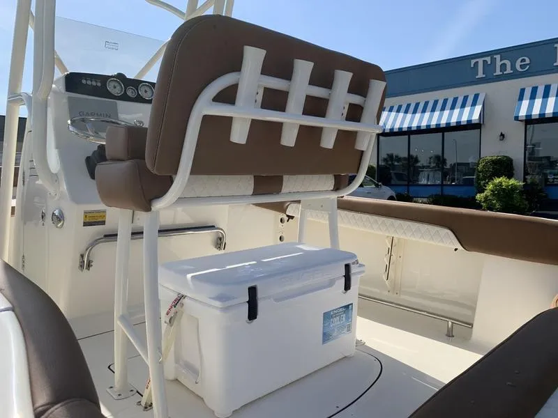 Slide: The Image of 2025 Pioneer ISLANDER 202 boat interior with seating and cooler, near a building with striped awnings. - 12