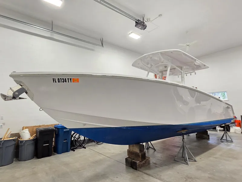 Slide: The Image of 2023 Jupiter 30 boat in garage, white hull, blue bottom, on stands. - 0