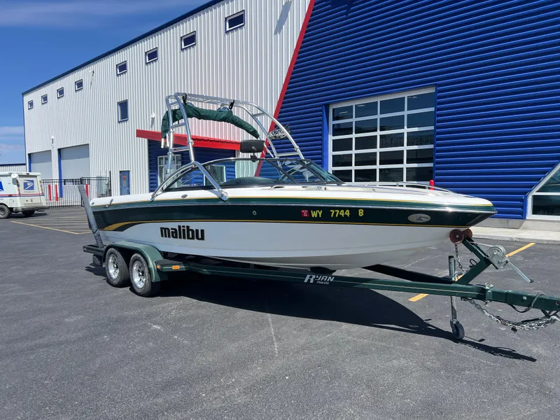 Slide: The Image of 2003 Malibu 23 XTi boat on trailer, parked outside a blue and white building. - 3