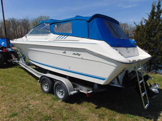 Slide: The Image of 1990 Sea Ray 260 Overnighter boat with blue canopy on a trailer, parked on grass. - 3