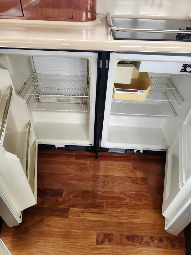 Slide: The Image of 2004 Sea Ray 480 Sedan Bridge kitchen with open fridge, wooden floor, and sink. - 23