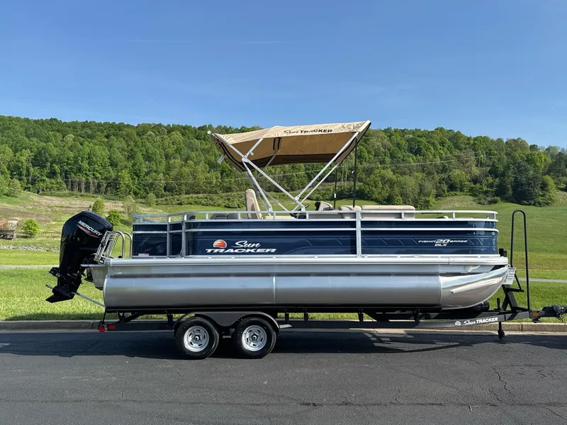 Slide: The Image of 2025 Sun Tracker Fishin' Barge 20 DLX pontoon boat on trailer, scenic background. - 2
