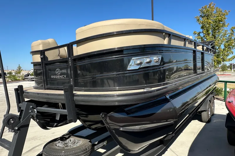 The Image of 2024 Regency 230 LE3 pontoon boat on trailer, black exterior, beige seating. - 1