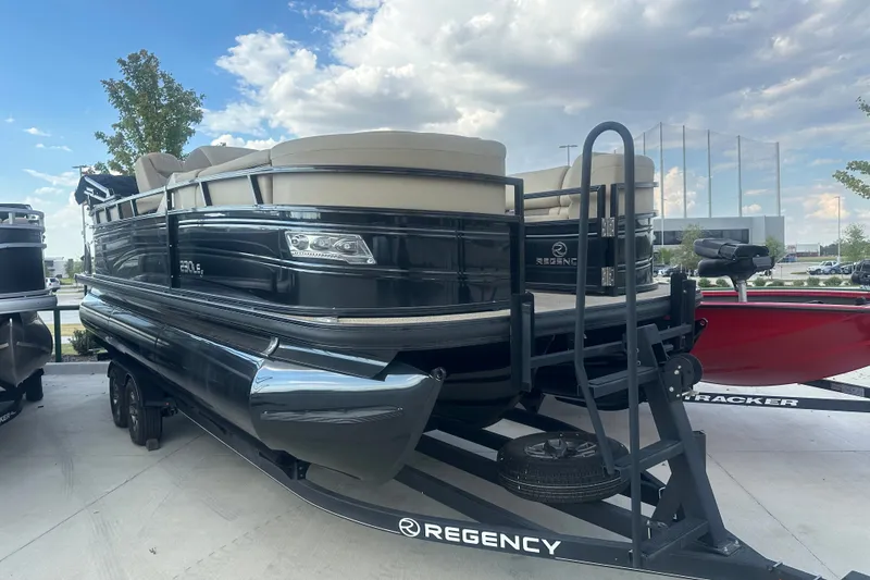 Slide: The Image of 2024 Regency 230 LE3 pontoon boat on trailer under a partly cloudy sky. - 2