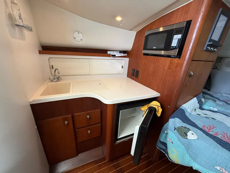 Slide: The Image of 1998 Tiara Yachts 2900 Open interior with kitchenette, sink, microwave, and cozy sleeping area. - 19