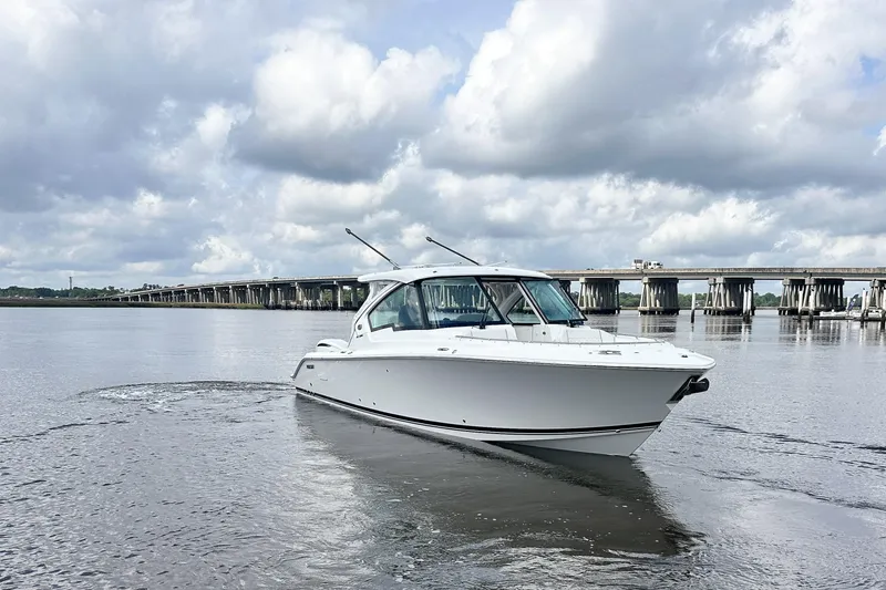 Slide: The Image of 2025 Pursuit DC 326 Dual Console boat on calm water with cloudy sky backdrop. - 2