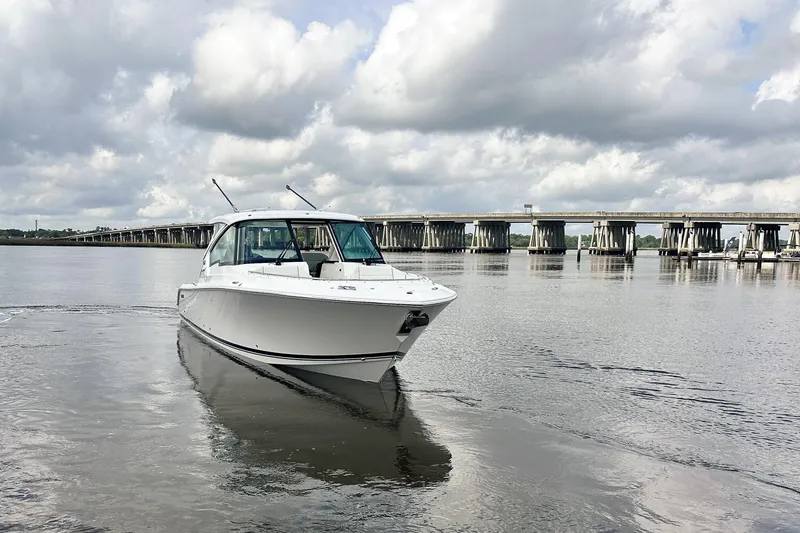 Slide: The Image of 2025 Pursuit DC 326 Dual Console boat on calm water near a bridge under cloudy skies. - 3