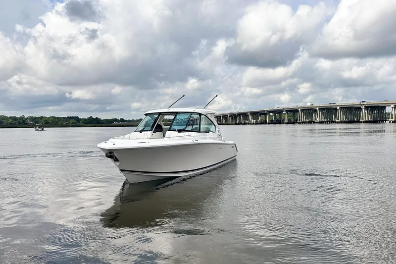Slide: The Image of 2025 Pursuit DC 326 Dual Console boat on calm water near a bridge under cloudy skies. - 5