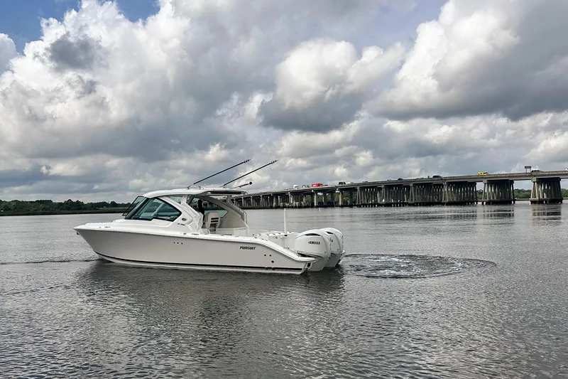 Slide: The Image of 2025 Pursuit DC 326 Dual Console boat cruising on a calm river under cloudy skies. - 9