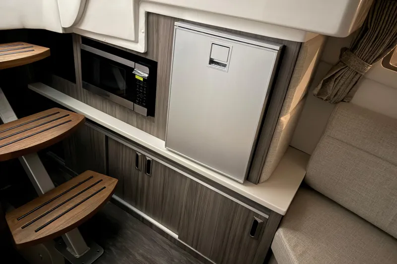 Slide: The Image of 2025 Sea Ray Sundancer 320 interior with microwave, fridge, and wooden steps. - 25