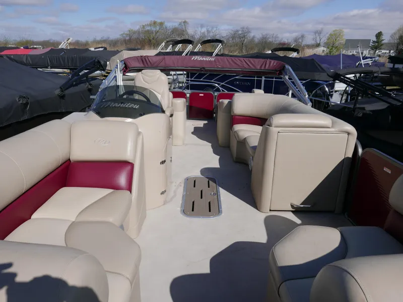 Slide: The Image of 2015 Manitou Oasis pontoon boat with beige and red seating, docked under a cloudy sky. - 10