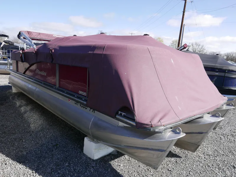 Slide: The Image of 2015 Manitou Oasis pontoon boat with maroon cover, parked on gravel. - 3